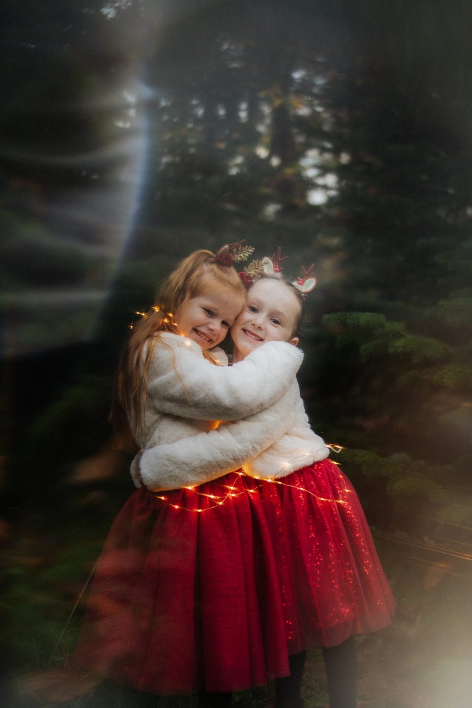 Deux petites filles qui se câlinent entourées de guirlandes lumineuses, capsules de Noël par Cathy Line