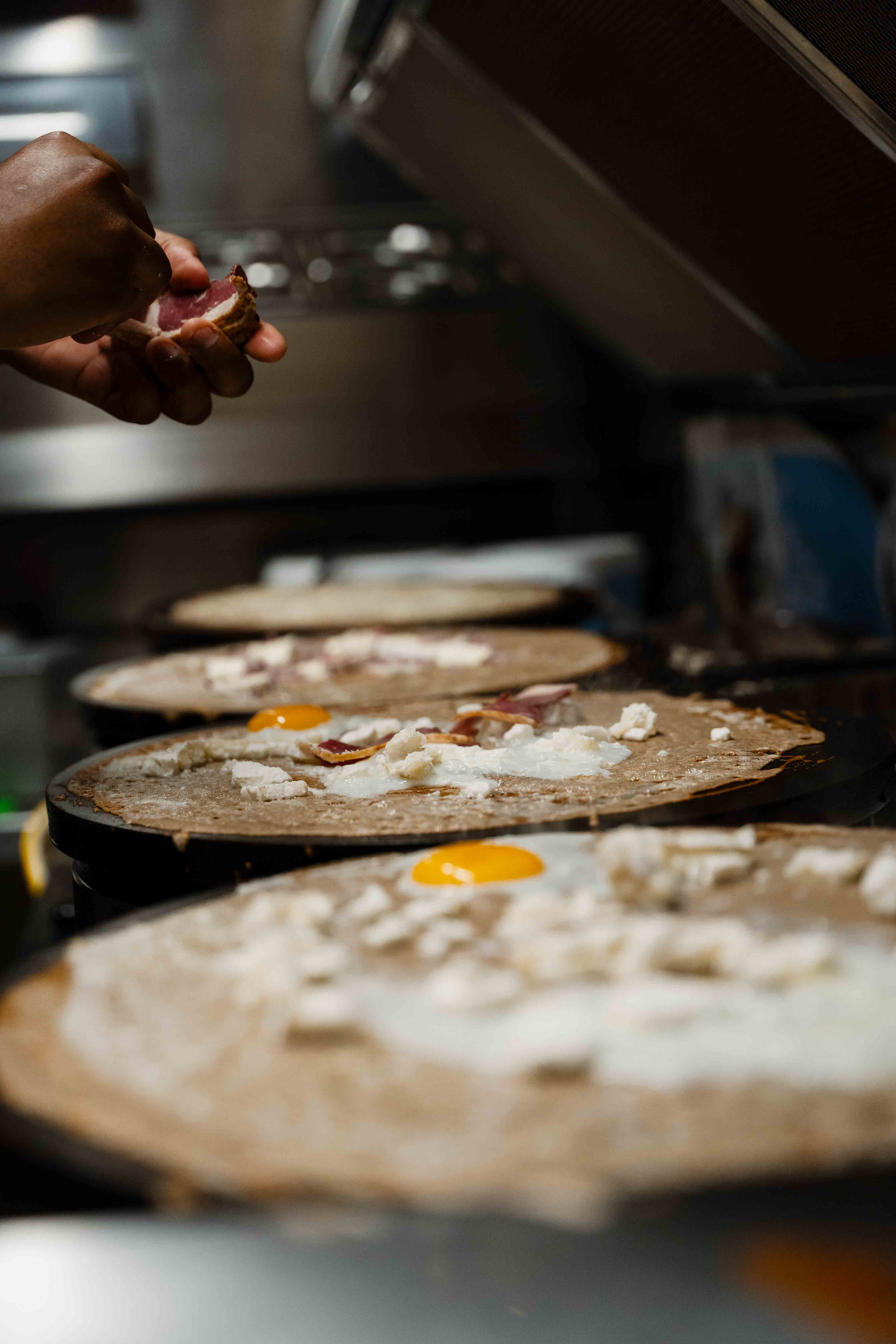 Galettes complètes en cuisson sur les billigs, œuf et lardons