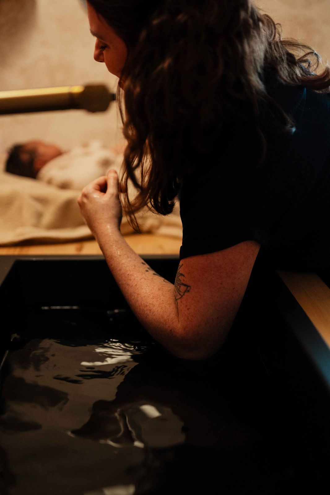 Anne-Laure vérifie l'eau du bain, bébé endormi derrière elle