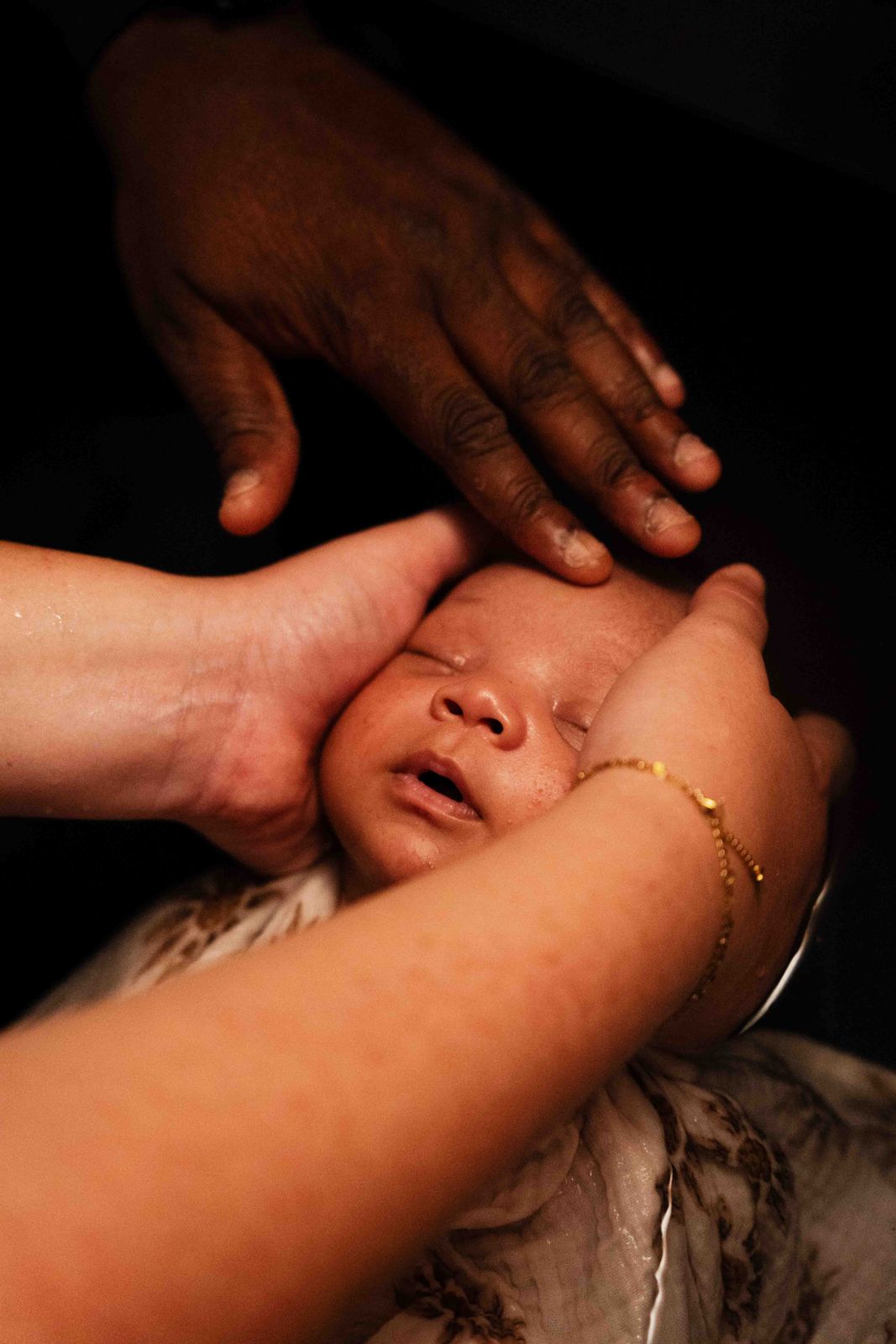 Les mains du papa, de la maman et d'Anne-Laure autour du visage du bébé